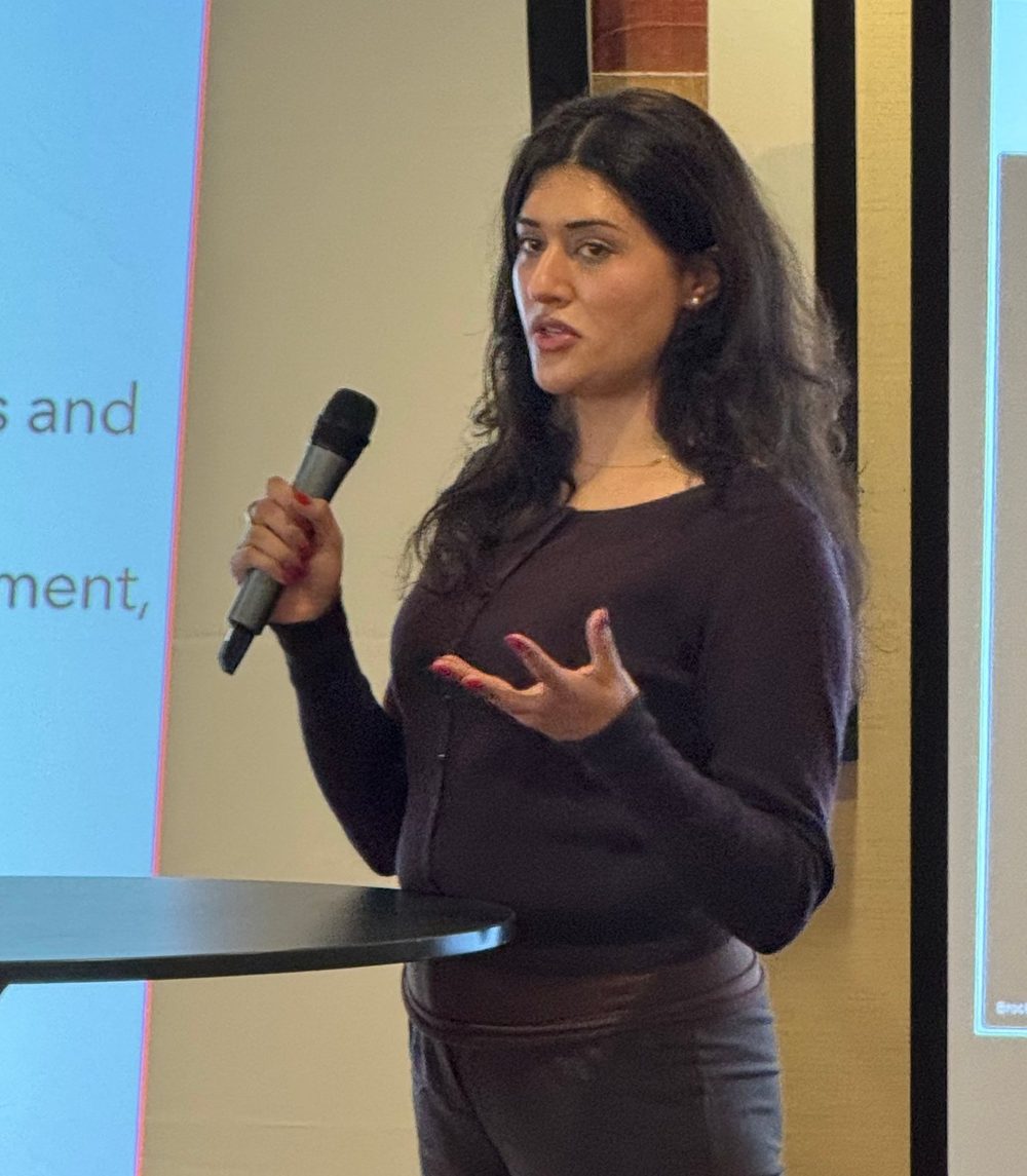 Prabhjot Sangha speaking with a microphone in front of a presentation slide